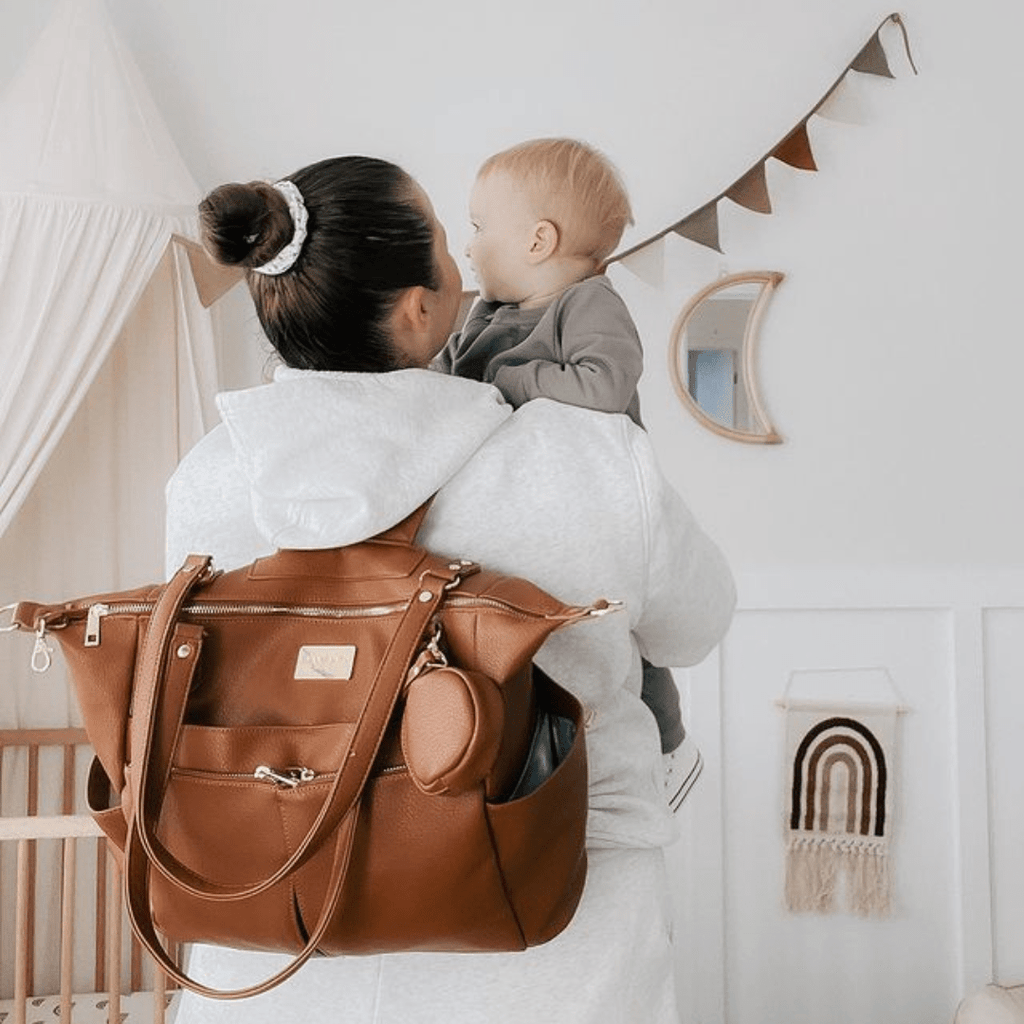 Sofia Nappy bag in tan faux leather - nappy bagworn as a backpack by woman holding baby bambino bagz